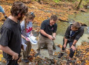 Four people looking at glacial sediments beside a creek